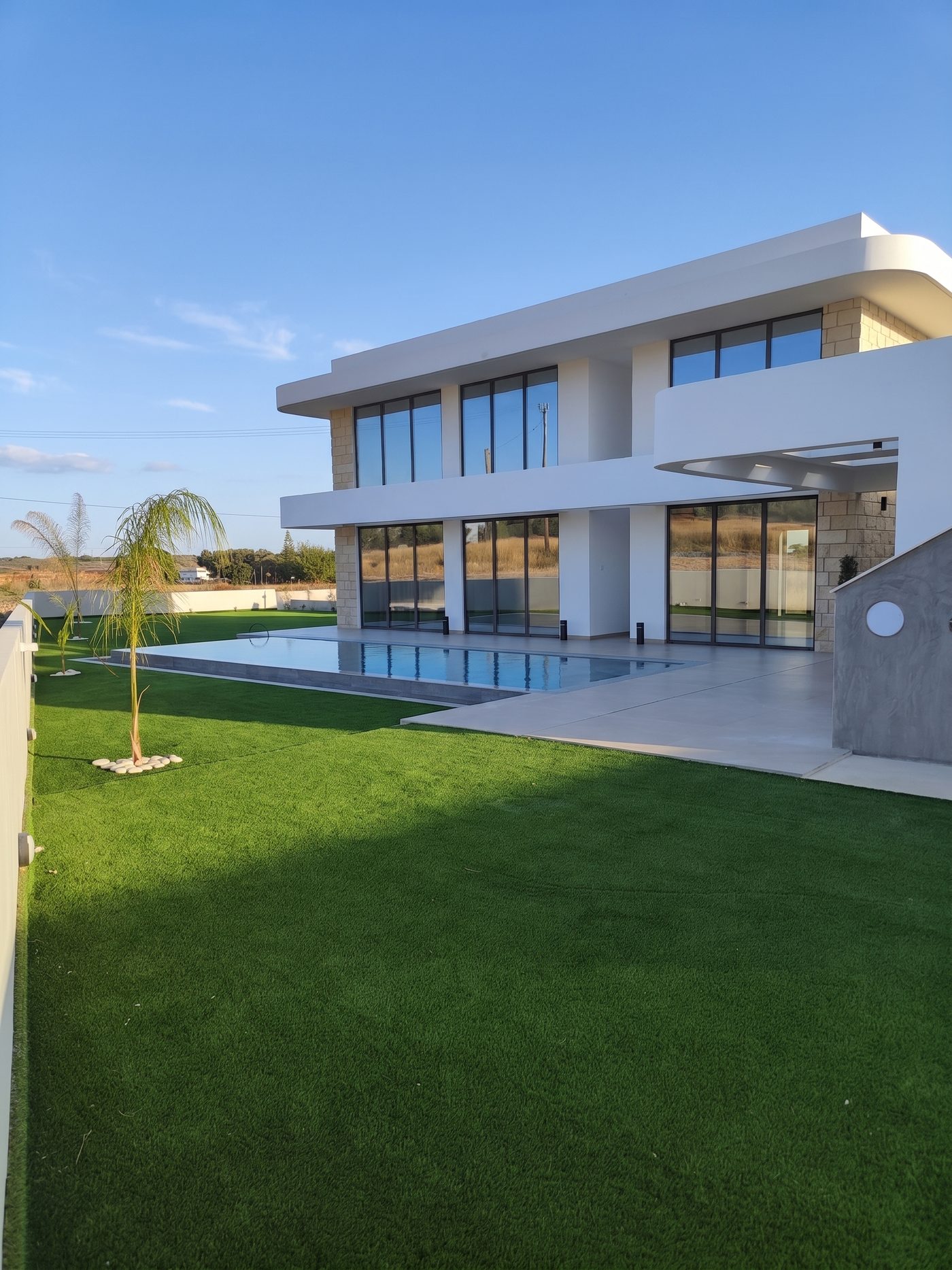 A two-storey villa with a lap pool along its terrace and a lawn beyond